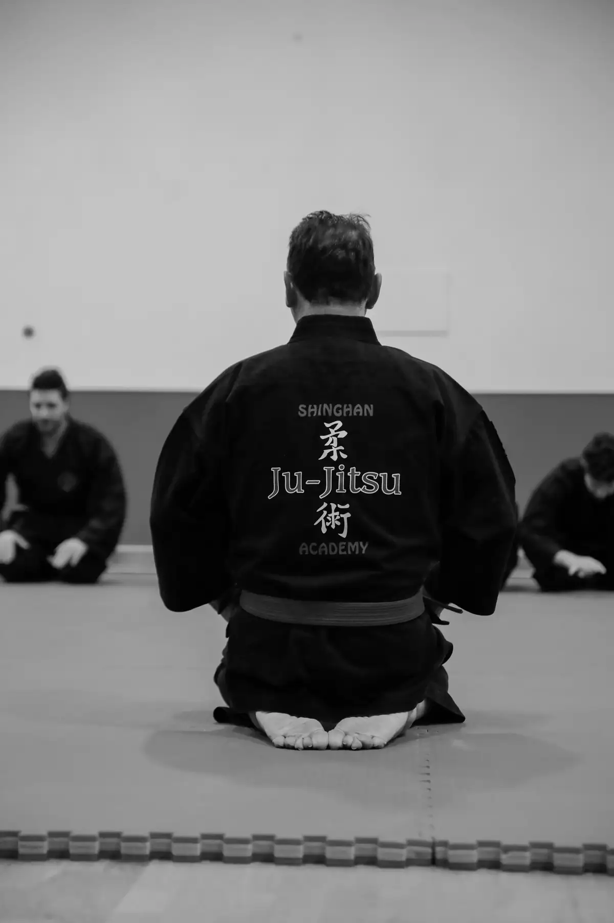 Allievo inginocchiato di spalle con il kimono nero «Shinghan Ju-Jitsu Academy»